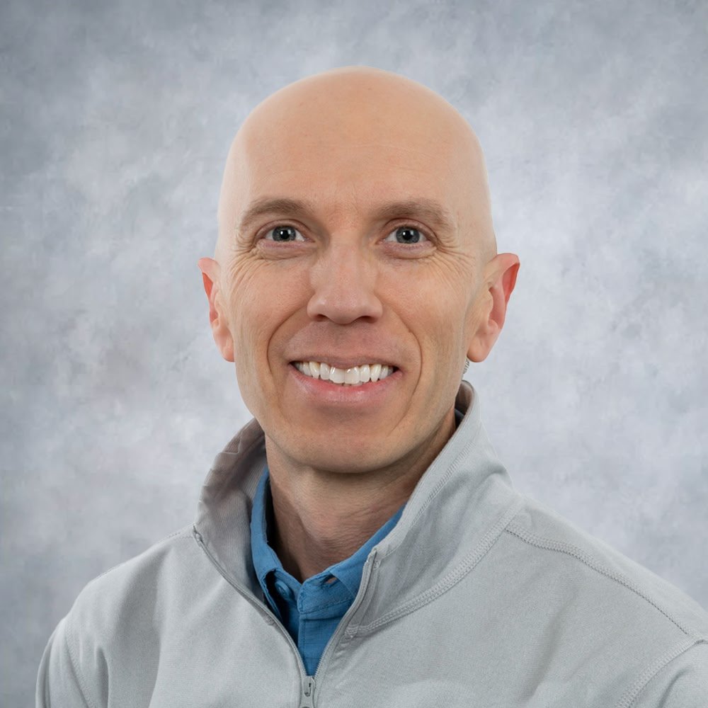 A headshot of man in front of a neutral backdrop