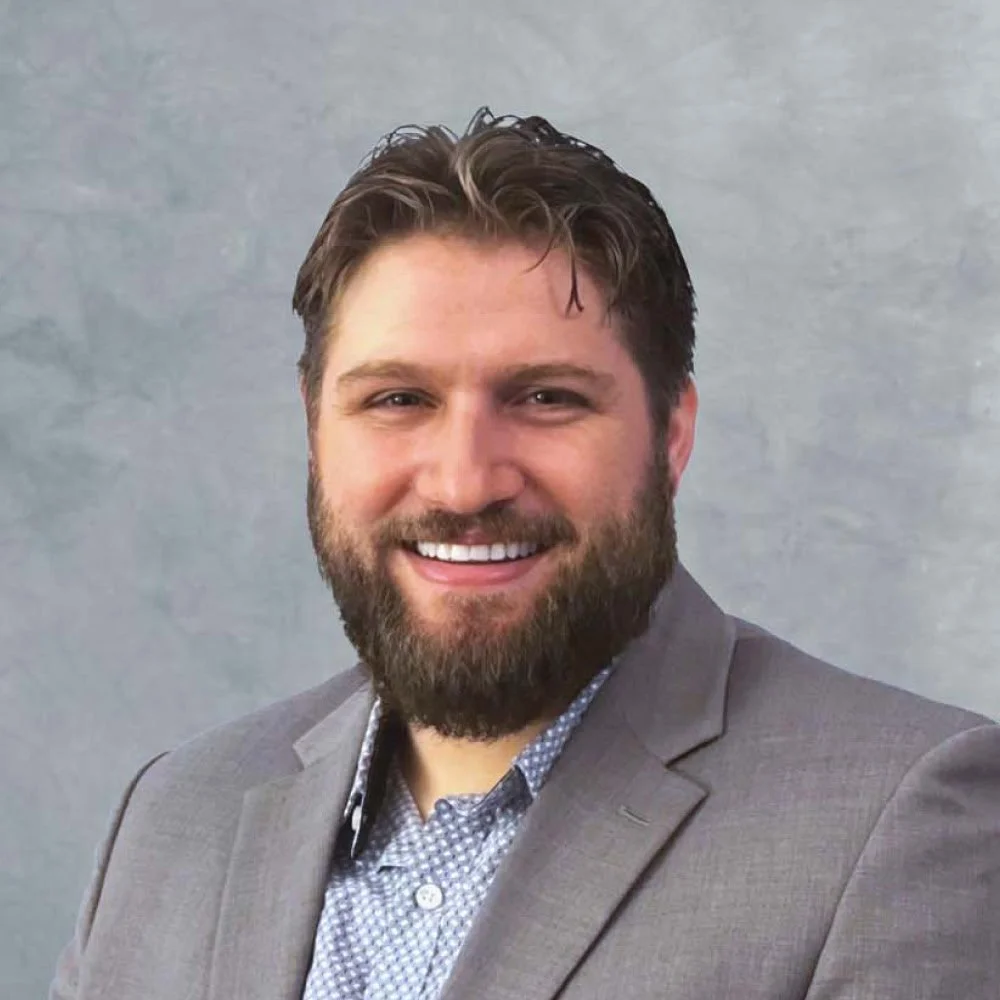 A headshot of man in front of a neutral backdrop