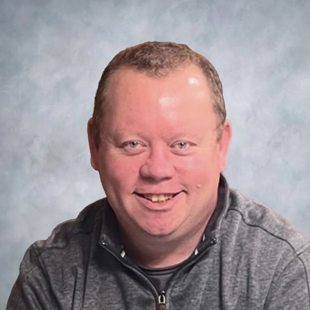 A headshot of man in front of a neutral backdrop