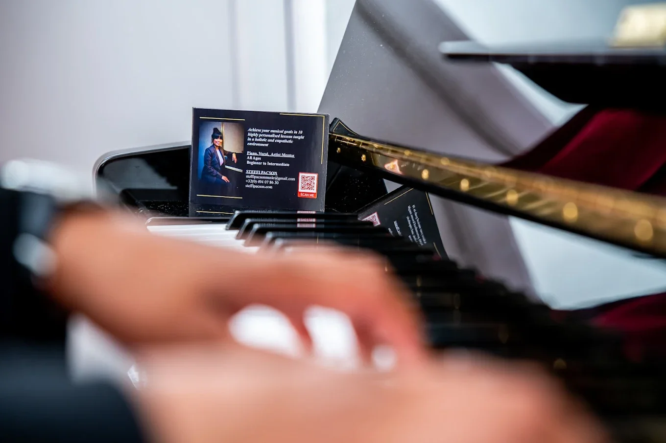 Close-up of a person's hands playing a grand piano, with business cards placed on the piano keys in the background. The cards feature a woman in professional attire and contact information.