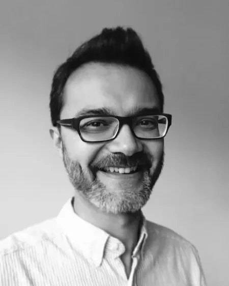 Black and white photo of a smiling man with glasses, facial hair, and short dark hair, wearing a collared shirt.