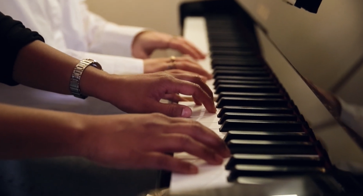 Two people playing piano together, focusing on their hands on the keyboard.