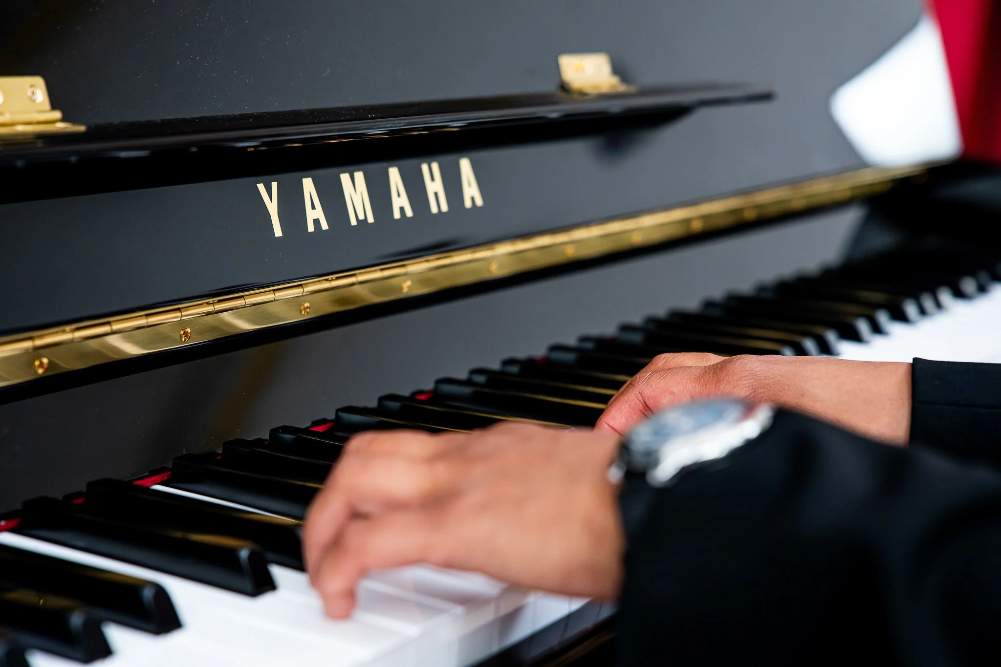 Close-up of a person's hands playing a Yamaha black upright piano, with focus on the keys and the brand name.