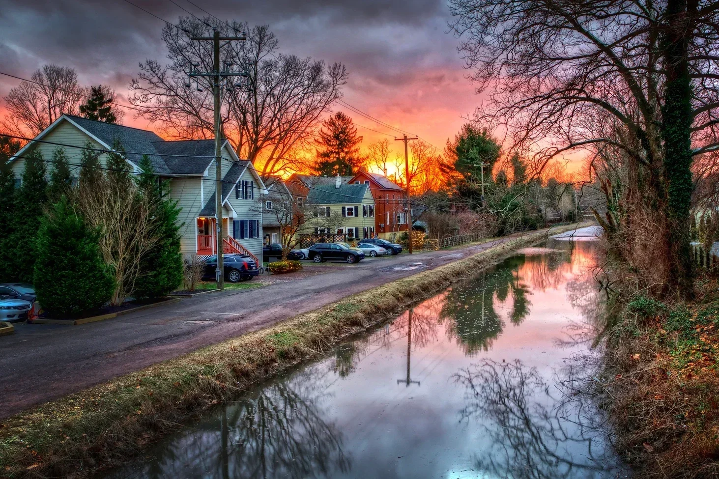 Sunset over a residential neighborhood alongside a canal with trees and parked cars.