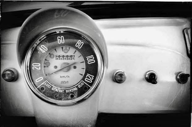 Close-up of a vintage car dashboard showing a speedometer, odometer, and fuel gauge, all in black and white.