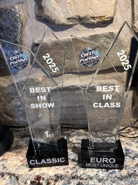 Two glass awards on a stone surface, one labeled "Classic" and the other "Euro Most Unique," both for 2025, recognizing "Best in Show" and "Best in Class," respectively, from Speed & Custom Awards.