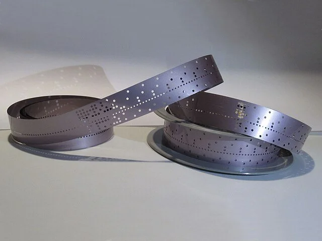 Two rolls of silver perforated tape or film, punch tape
