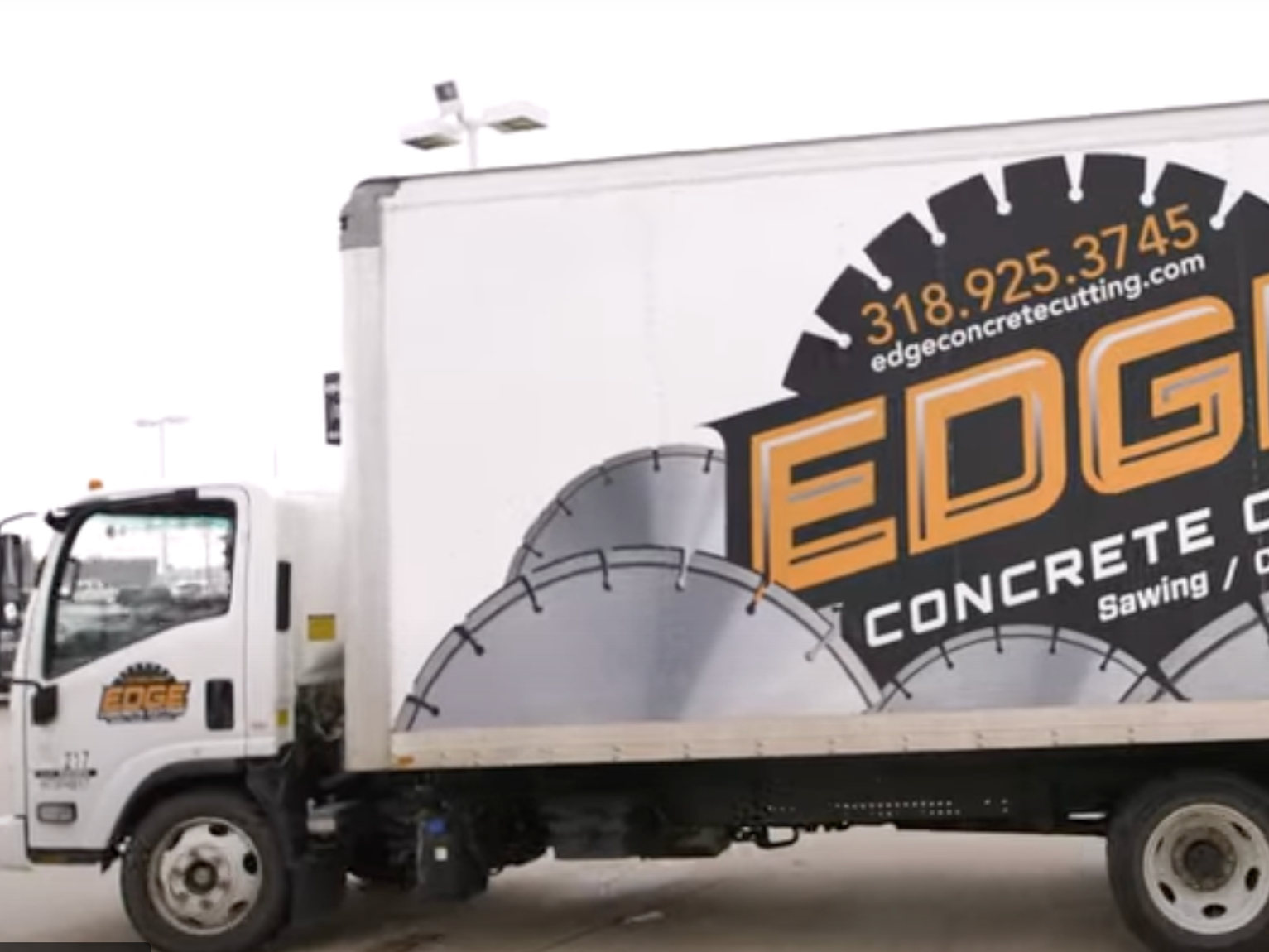 A white delivery truck with a sign for Edge Concrete Cutting, featuring a large circular saw blade graphic and contact information.