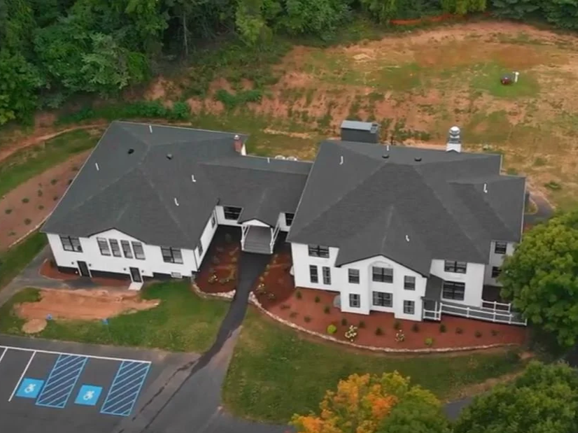 Exterior view of healthcare project Paramount Wellness Center, surrounded by green trees and landscaped yard, located near a parking lot with accessible parking spaces.