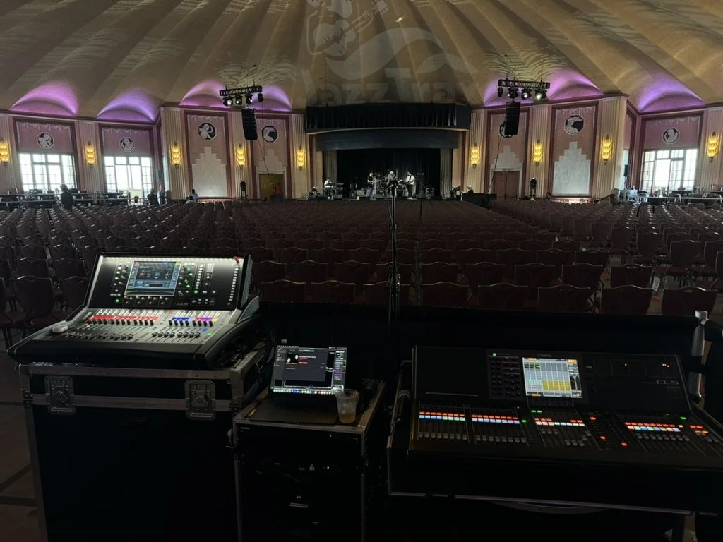A dimly lit backstage storage room illuminated by blue light, with chairs, tables, and storage cases.