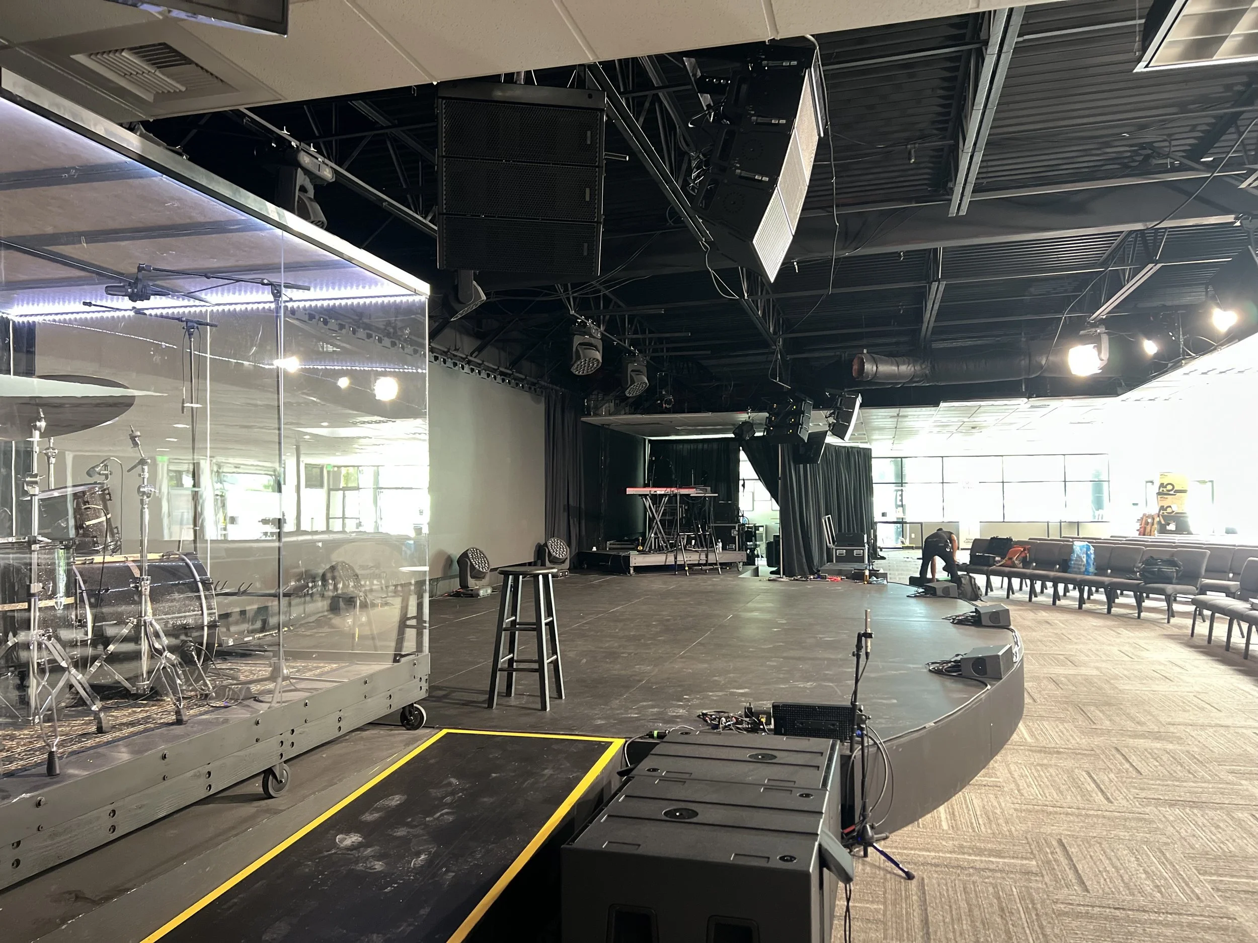 A man in a baseball cap and glasses working at a digital audio mixing console in a recording studio, smiling and looking at the equipment.