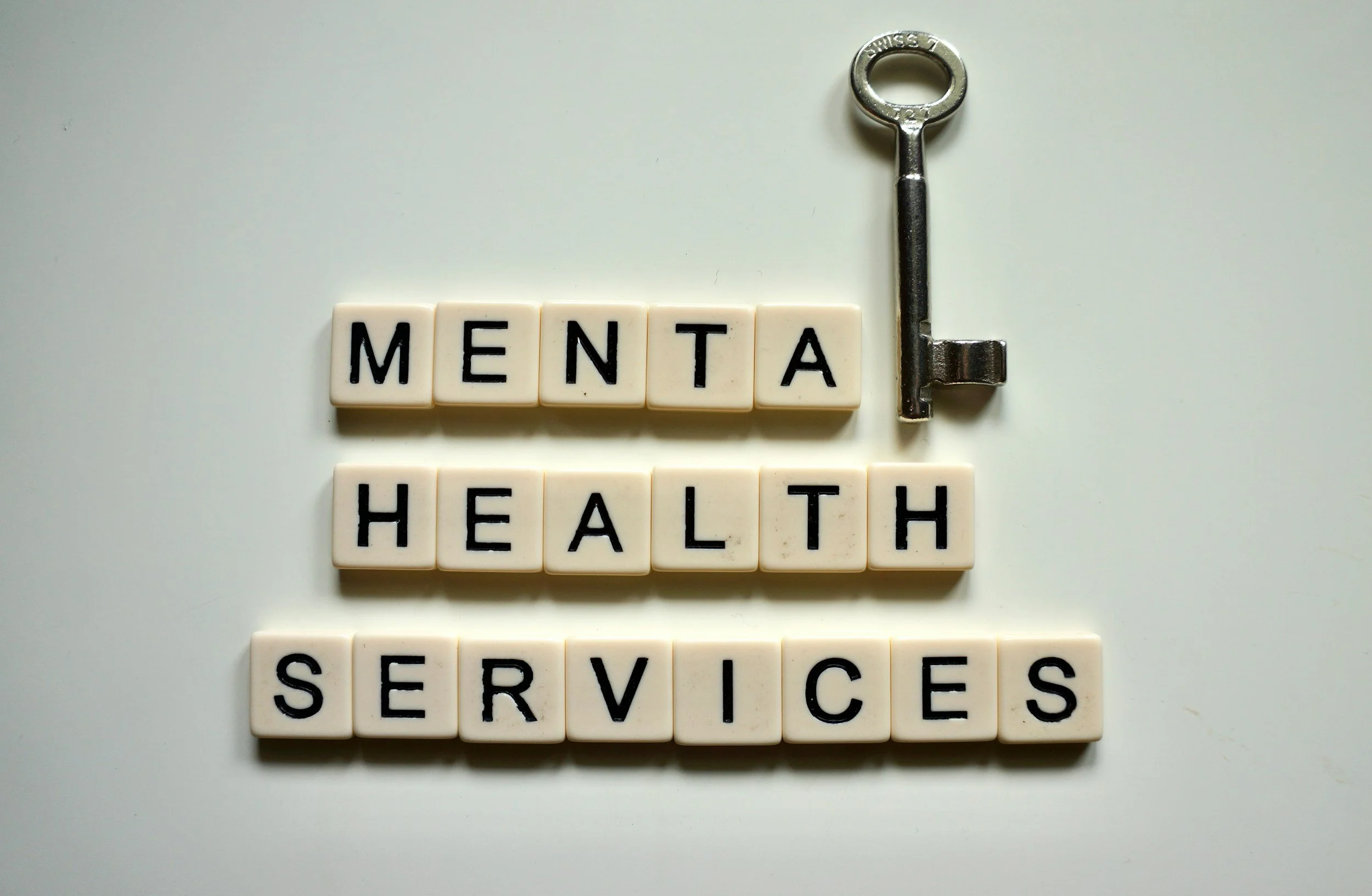 Scrabble tiles spelling 'MENTAL HEALTH SERVICES' with a key on a white surface.