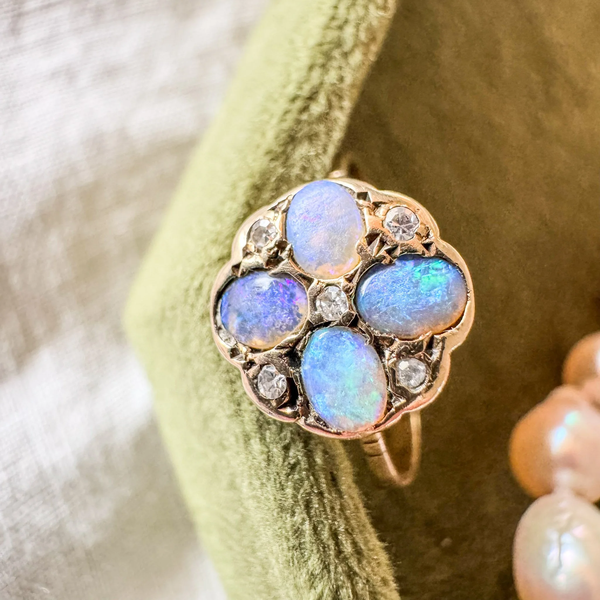 A gold ring with four opals and six small diamonds on a green fabric surface.