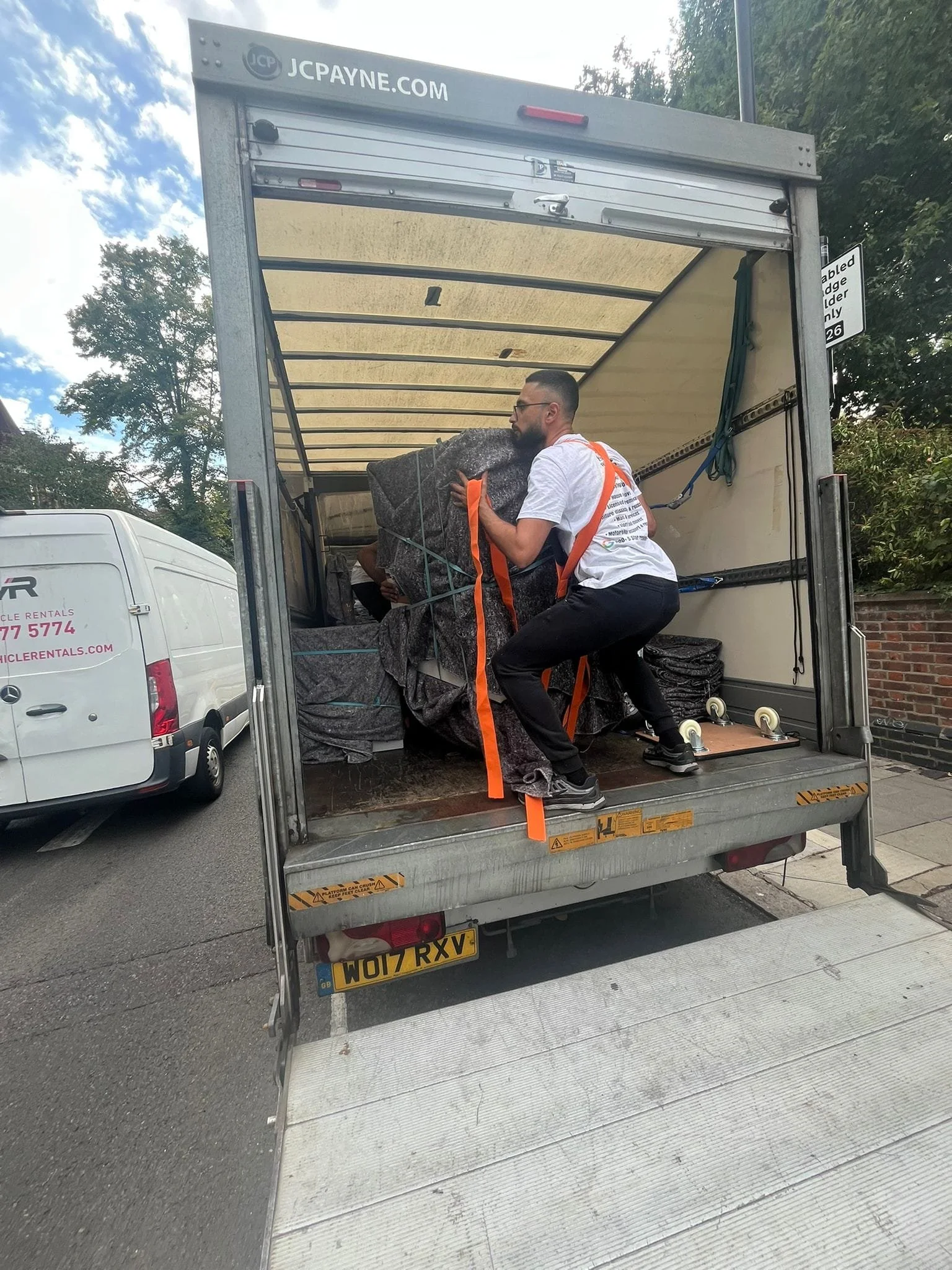 2 Movers from Ready to go house movers and removals using orange shoulder lifting straps to help lift a heavy piece of furniture that is wrapped around in a removal blanket to be loaded into their Luton van for a clients house move in North West Lond