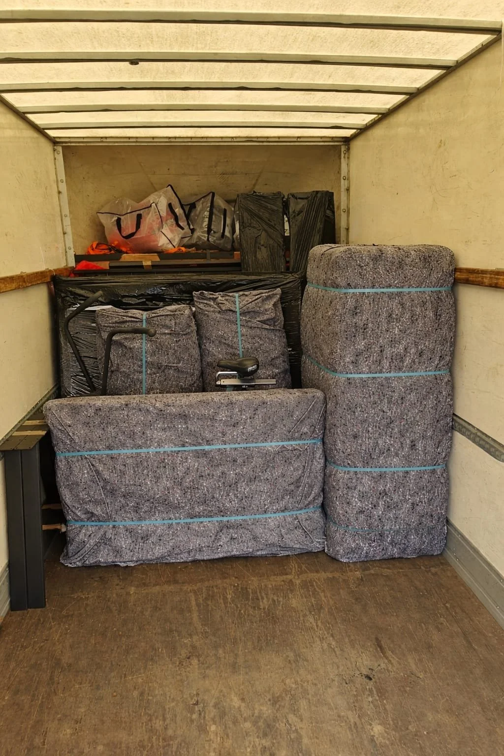 The back of a moving truck filled with household items including mattress pads, a rolled-up mattress, and several plastic bags.