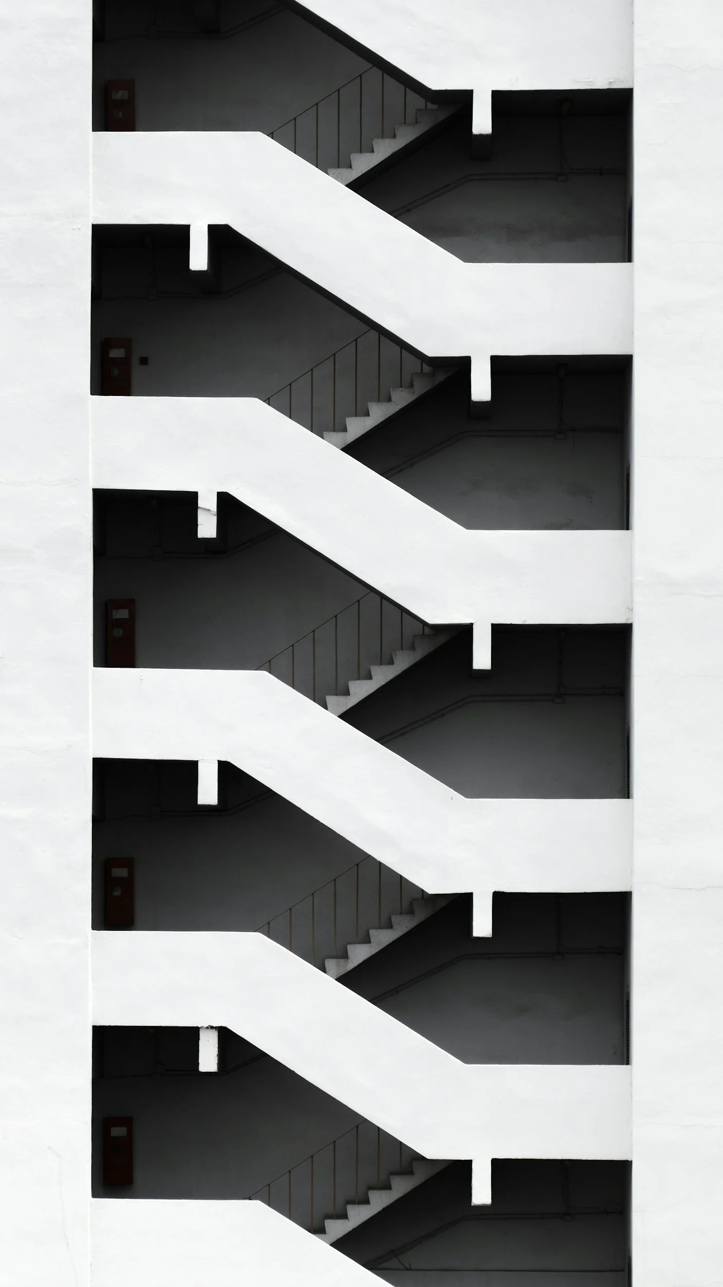 A black and white photo of a building's exterior stairwell with diagonal stairs and railing, viewed from the side.