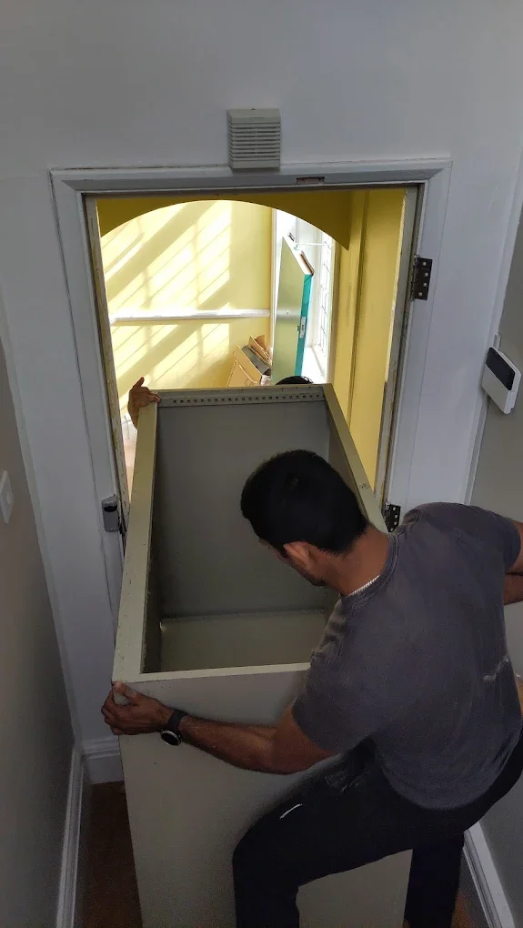Man lifting a large cabinet through a doorway to an upstairs room.