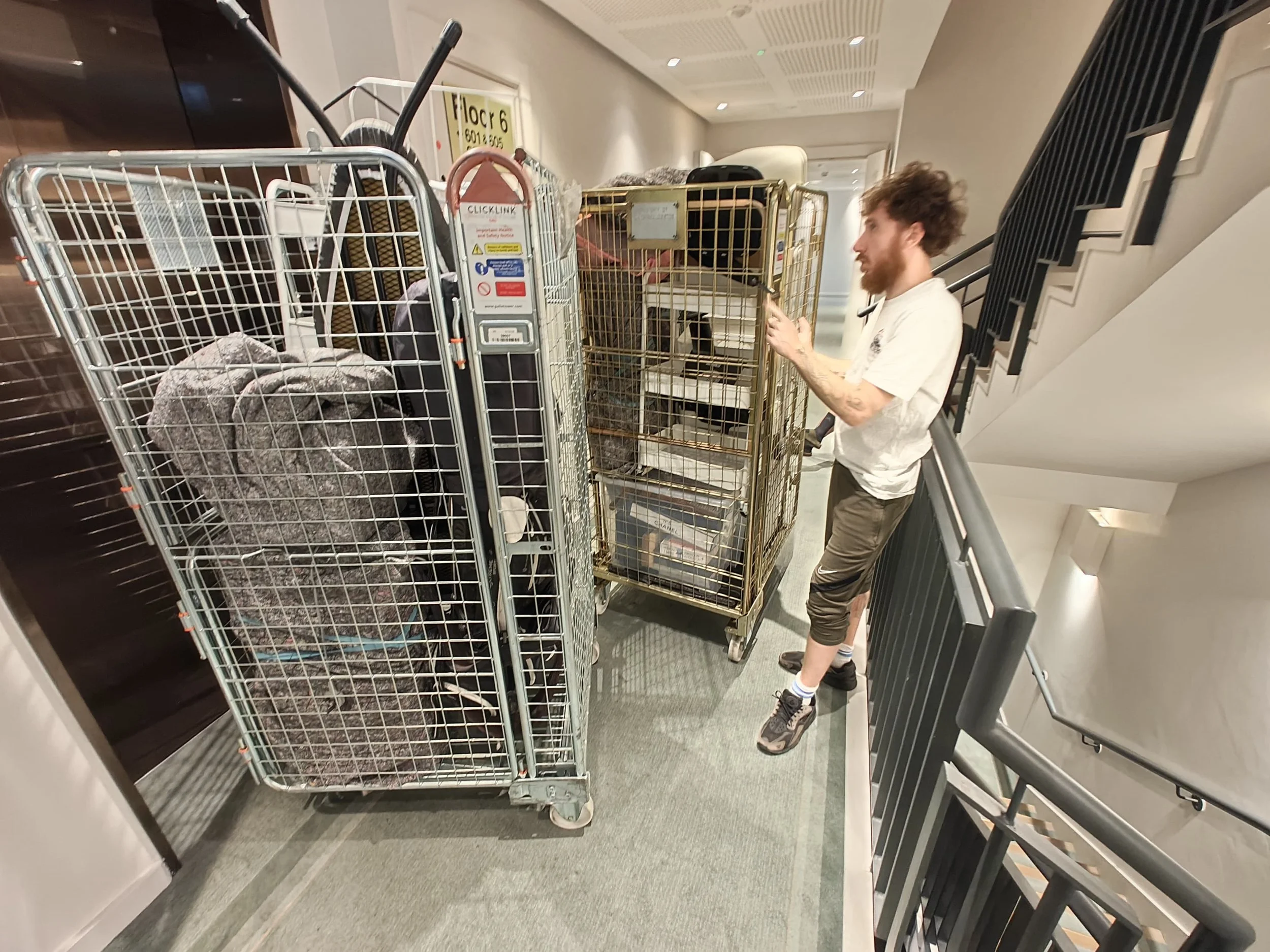 Movers from Ready To Go House Movers And Removals waiting for a lift with their roll cage carts filled with a customers items going down into their Luton van for loading. During a flat move in West London
