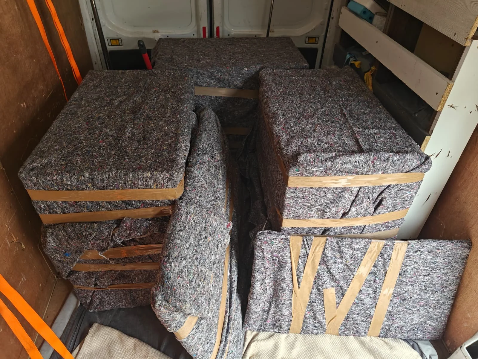 A cargo area with stacked boxes of used automotive seat cushions, secured with wooden slats and straps.