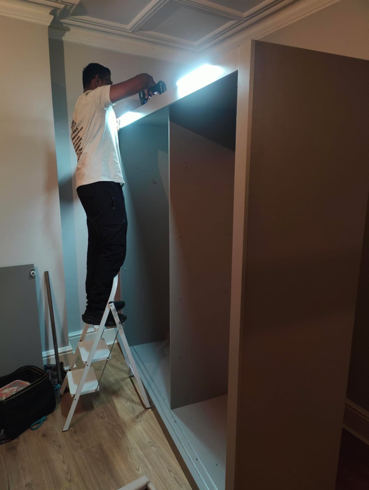 Wardrobe being put back together with light fittings on the top by a team member from Ready to go house movers and removals