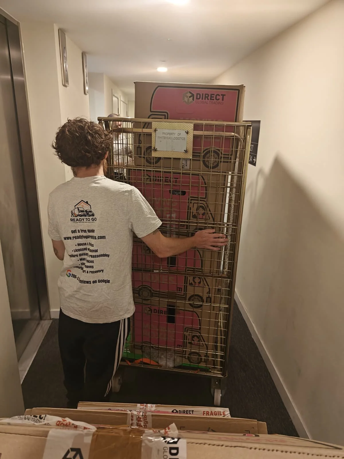Porter from Ready To Go House Movers And Removals waiting for a lift with their roll cage carts filled with a customers boxes going down into their Luton van for loading. These roll cage carts can hold many boxes compared to taking them by hand or sa