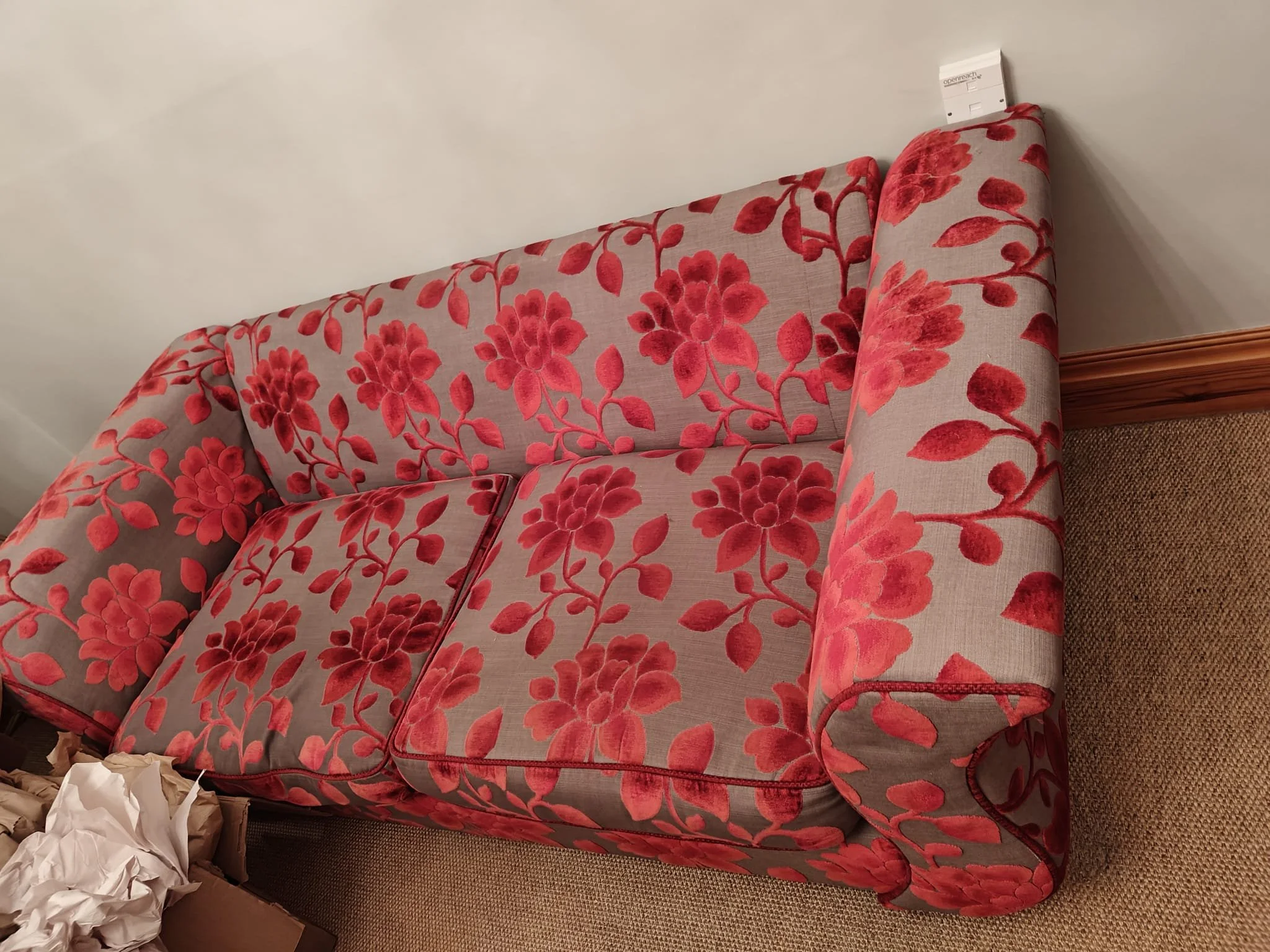 A floral-patterned sofa with a beige background and red flowers, situated in a room with beige carpet and white walls.