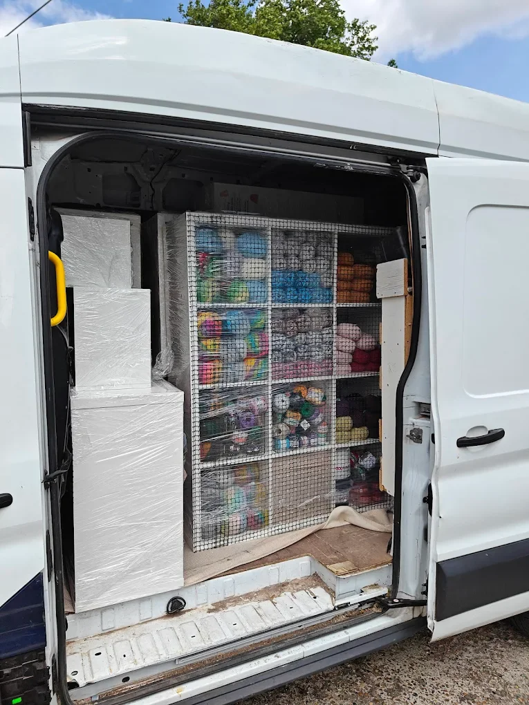 Interior of a delivery van with shelves stocked with yarn and craft supplies.