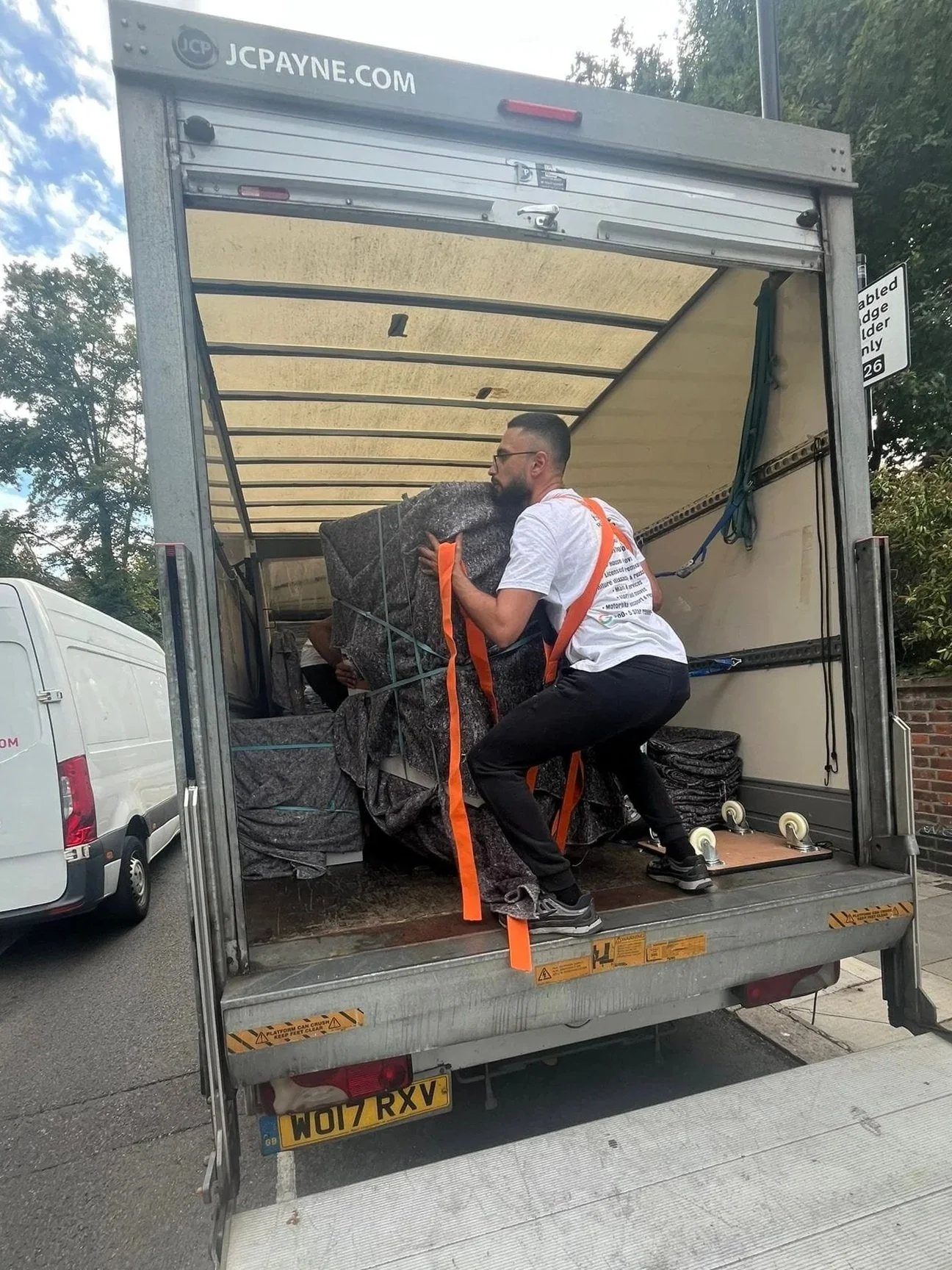 Man loading large wrapped furniture item into the back of a moving truck.
