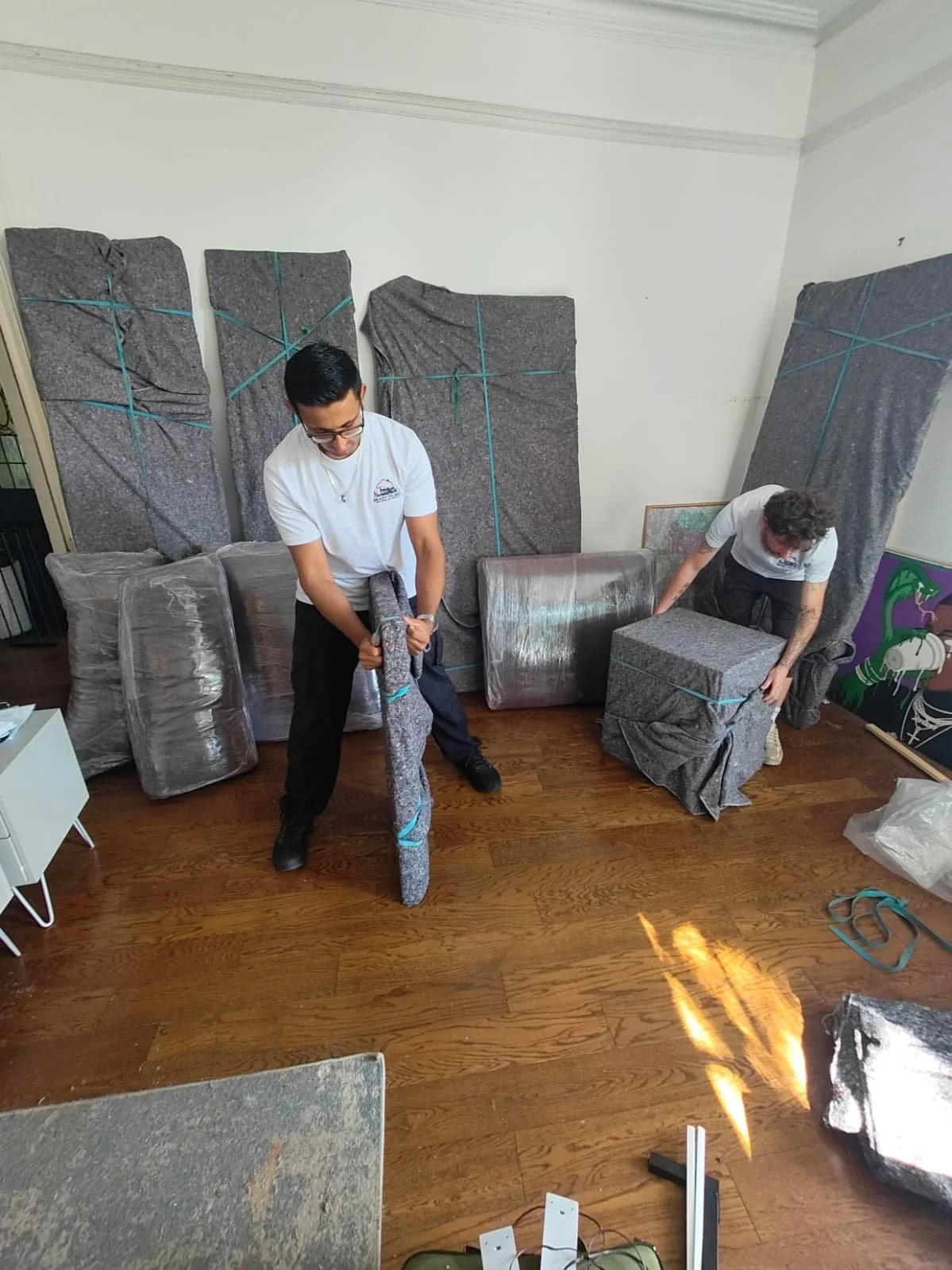 Removal workers from Ready to go house movers and removals wrapping a wardrobe and bedside table in removal blankets for protection.
