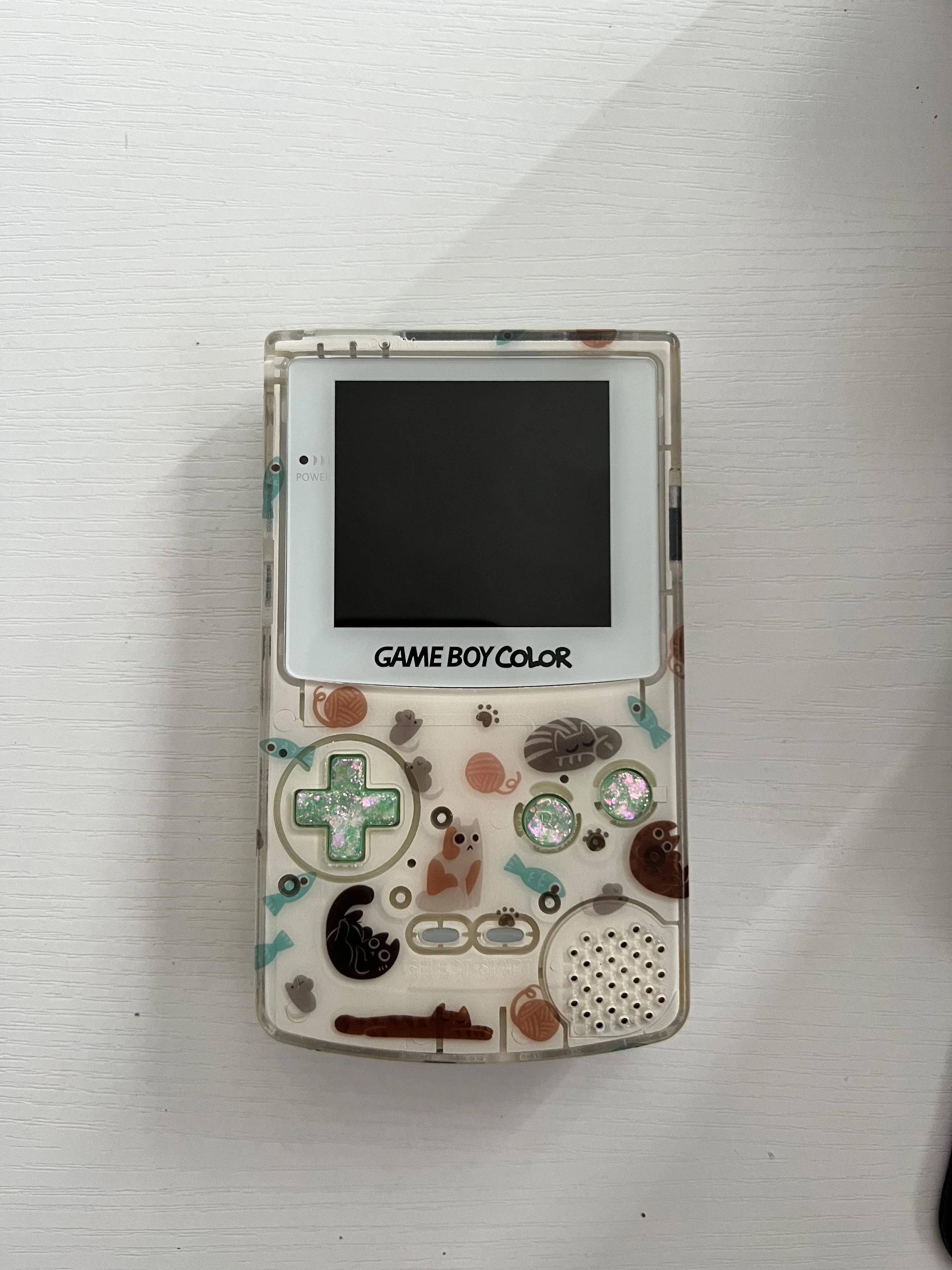 Decorated Game Boy Color with cat, fish, and yarn ball stickers on a white surface.