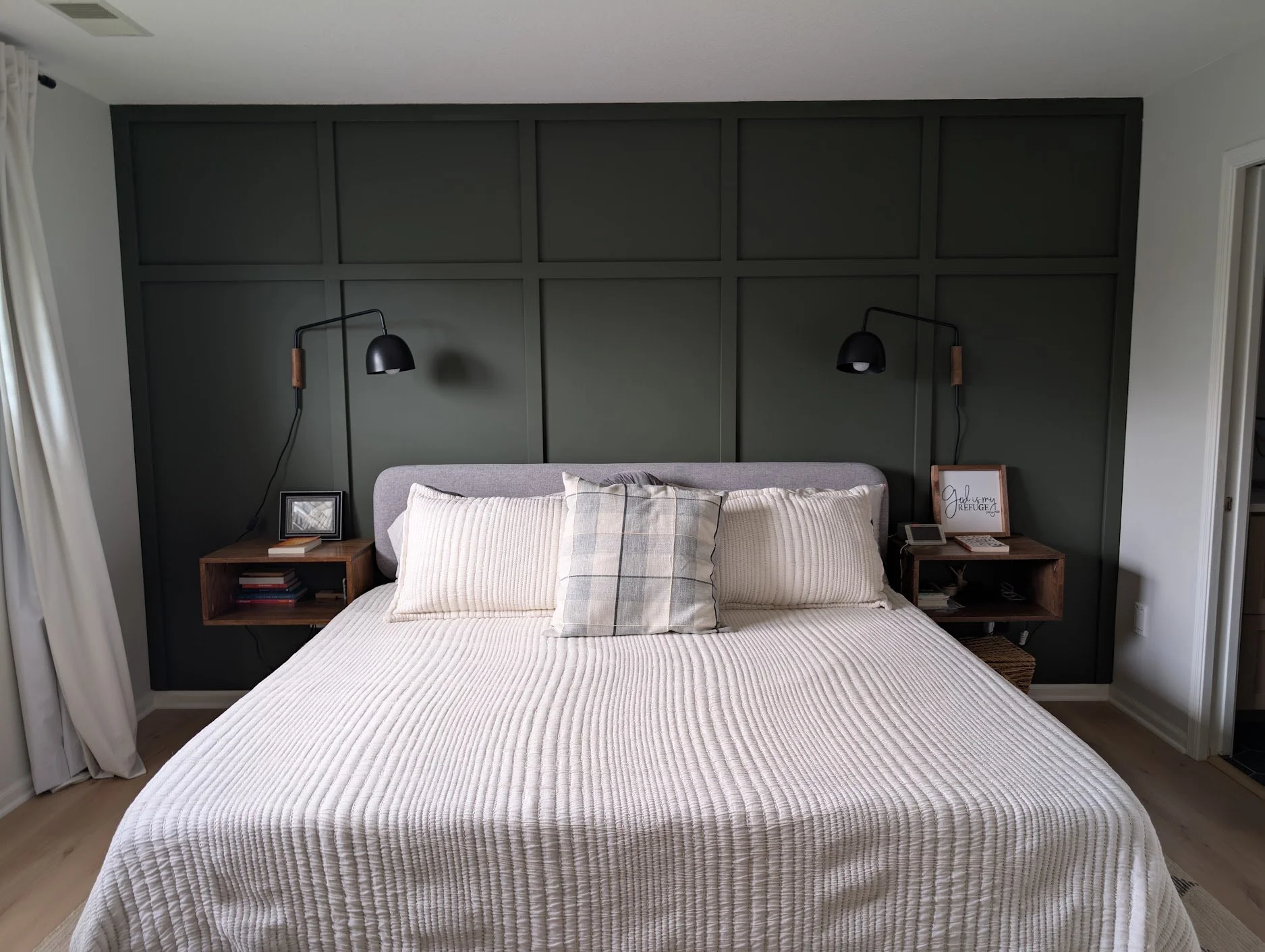 A dark green board and batten accent wall with two black wall-mounted reading lamps, and custom floating wooden bedside tables.