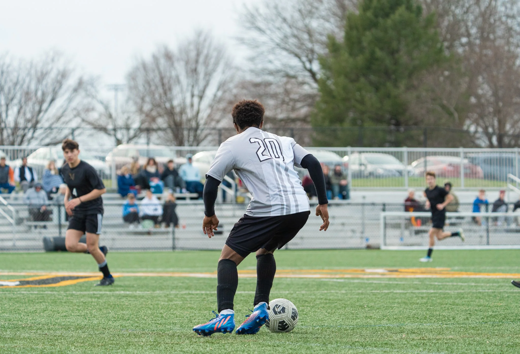 A soccer player with the number 20 on his jersey is about to kick the ball on a field with other players and spectators in the background.