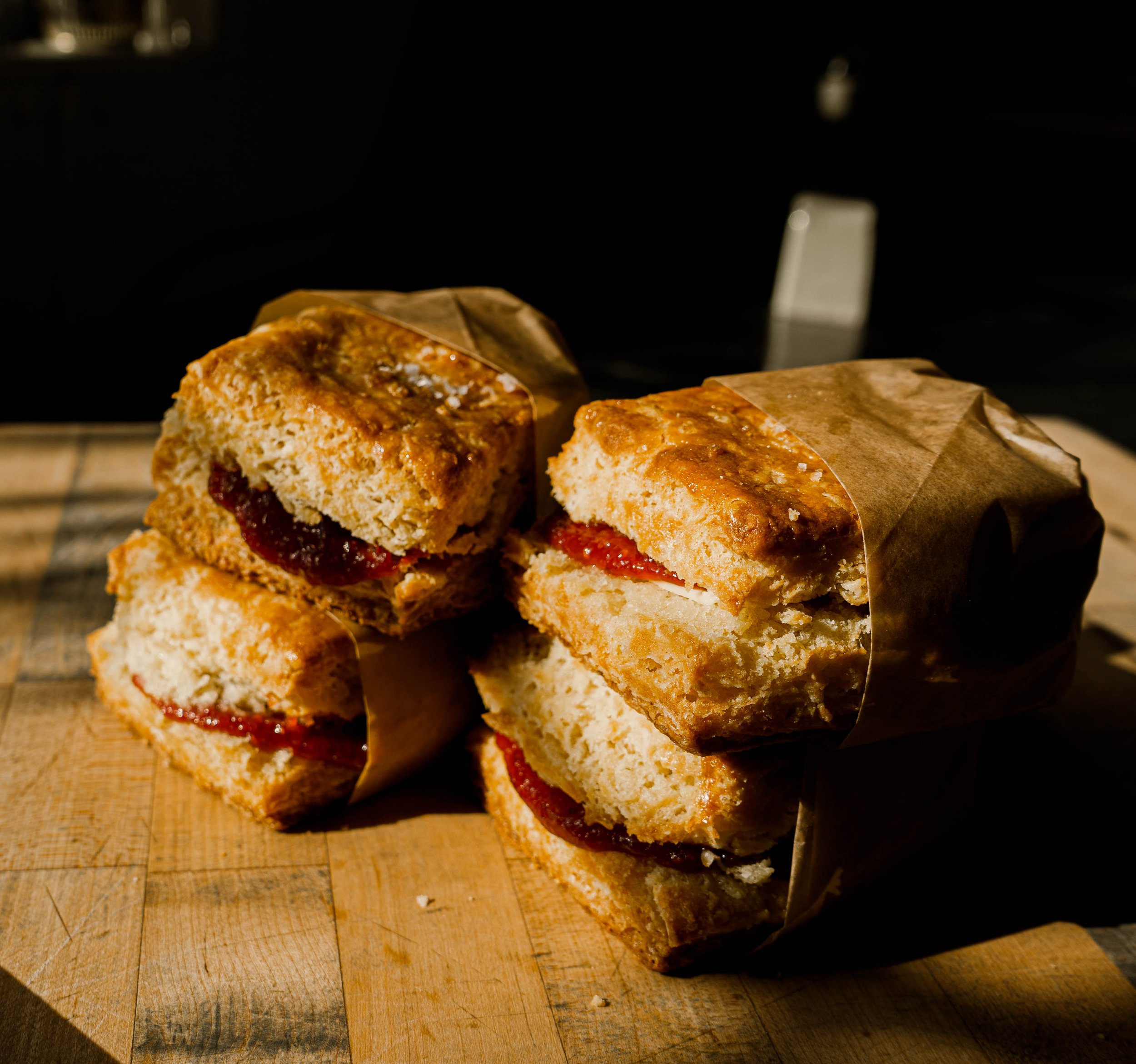 Close-up of two sandwiches wrapped in paper on a wooden cutting board, with toasted bread, tomato, and cheese visible.