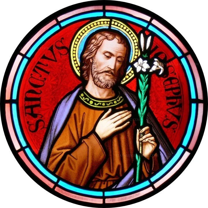 Stained glass window depicting Saint Jospeh, holding a lily flower and a staff, with a red background and a circular border.