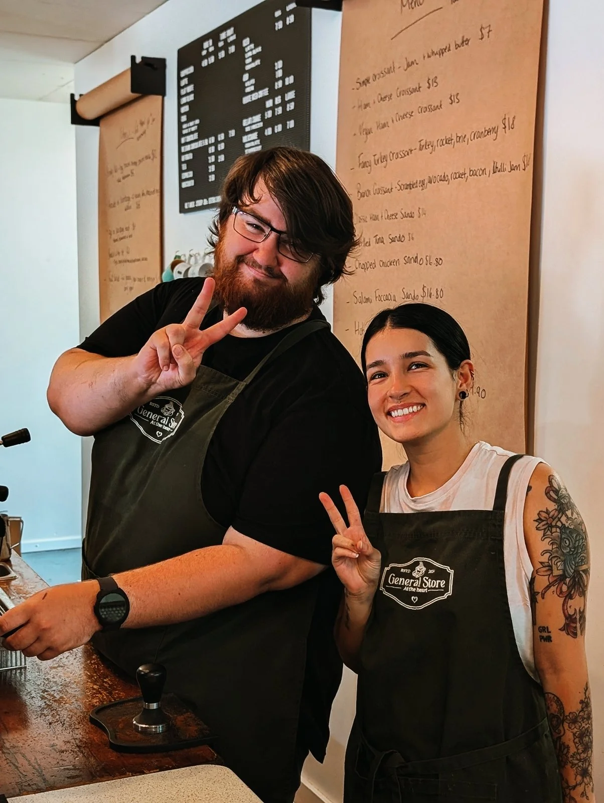 Two young women standing together, one holding a certificate of achievement, in a coffee shop or restaurant setting.