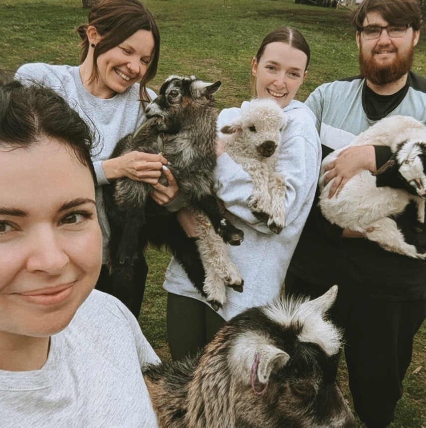 Five people holding various goats and a dog outside on grass.