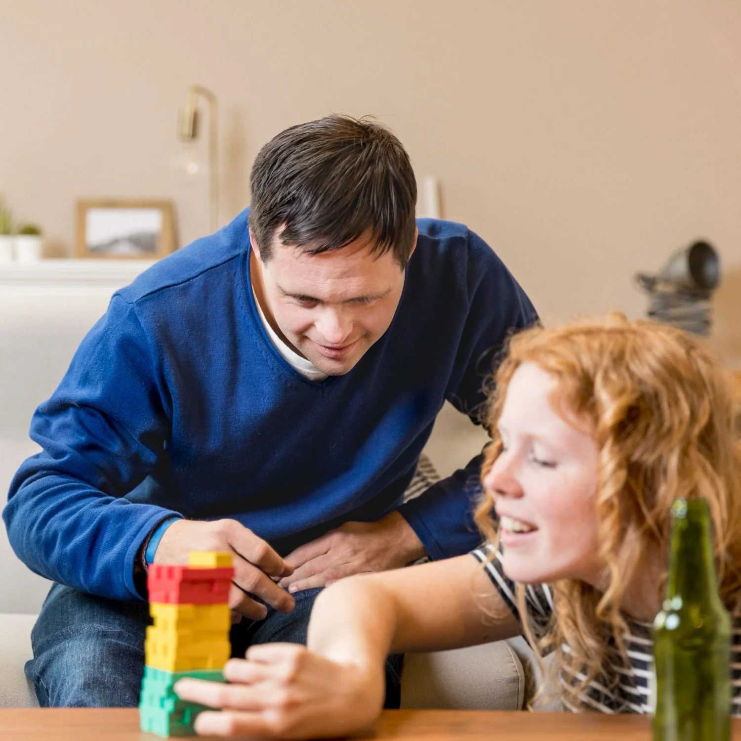 A man and a woman playing a game with colorful stacking blocks on a table.