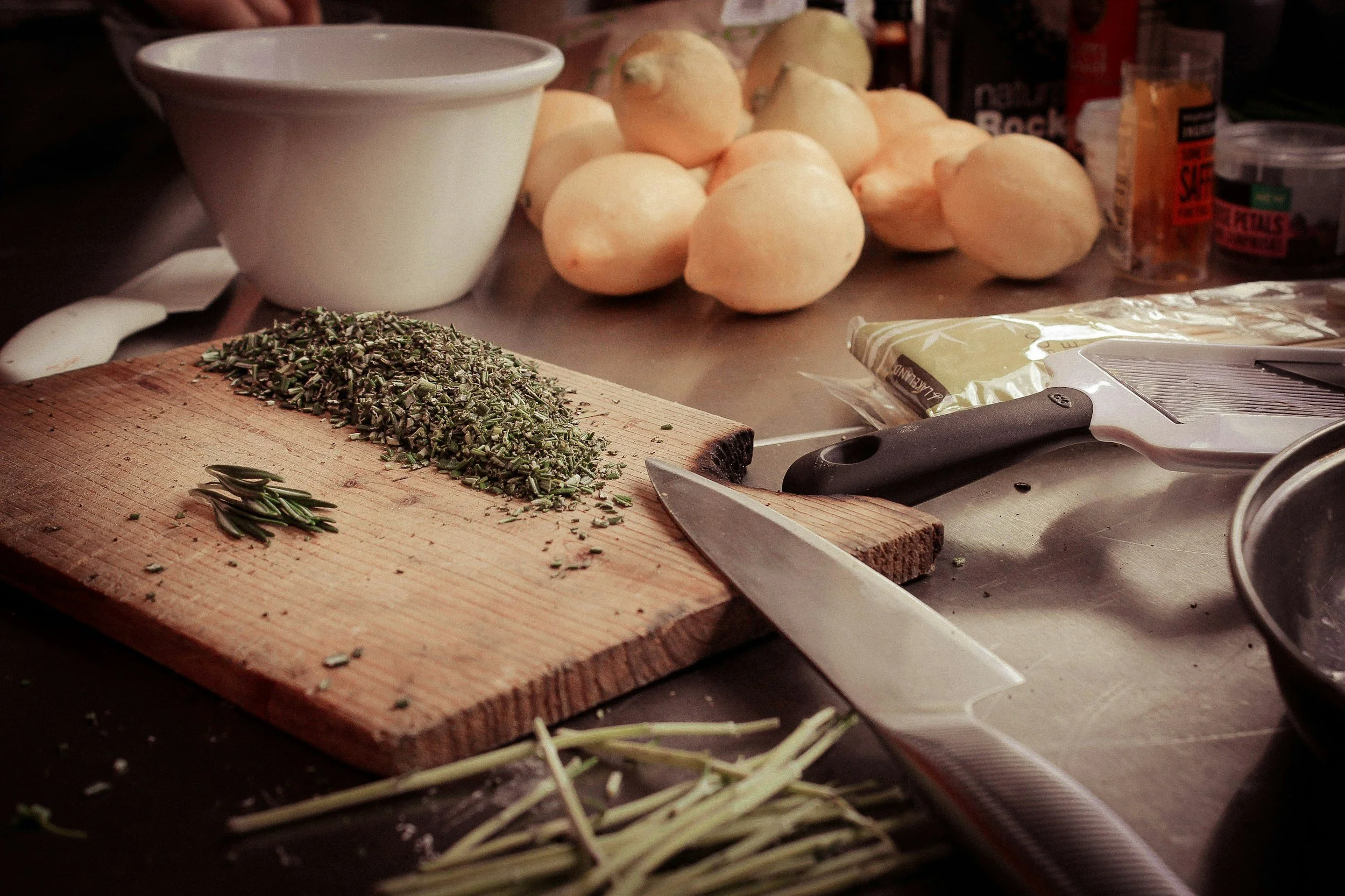 Herbes aromatiques sèches sur une planche en bois, oignons, un couteau et divers ingrédients culinaires sur une surface de cuisine. Ateliers culinaires afro-holistiques à Paris