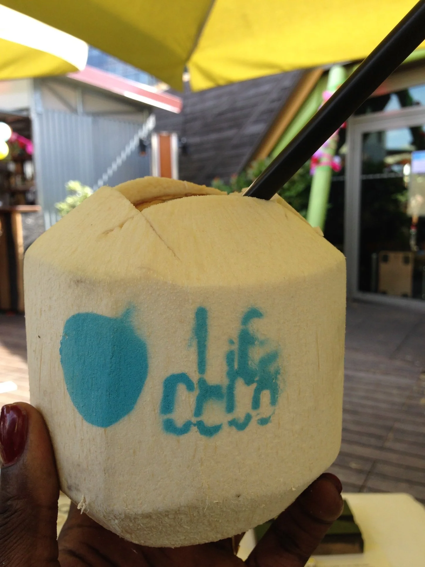 Une noix de coco fraîche avec une paille noire insérée, tenue par la main de Carine DJOB, Fondatrice de l'Atelier Holistique Urbain, Afro Nutrition, Nutrition Santé,  Éducatrice culinaire