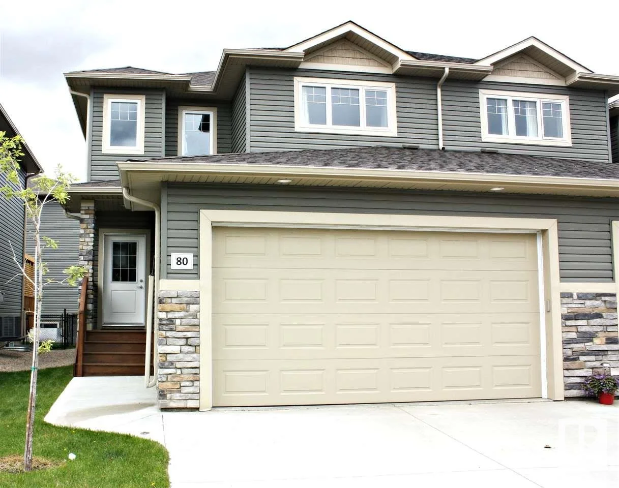 Front view of a two-story house with gray siding, a beige garage door, stone accents, and a small front porch with steps.