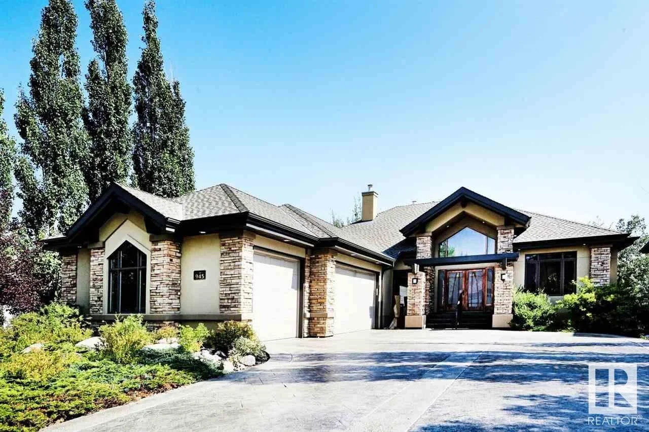 Front view of a large modern house with stone accents, a driveway, and landscaped yard, under a clear blue sky.