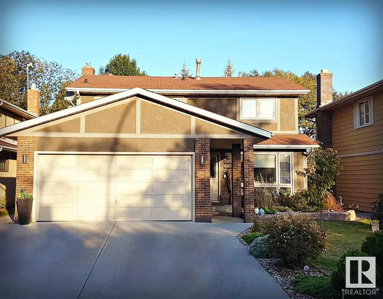 Front view of a two-story suburban house with a two-car garage, brick accents, and a well-maintained garden with bushes and plants.