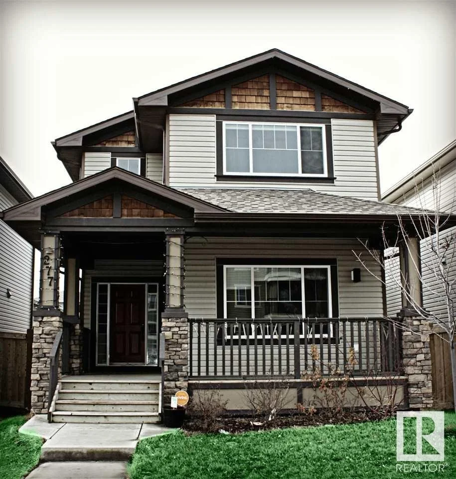 Two-story modern house with stone and siding exterior, front porch, and enclosed balcony, with well-maintained grass front yard.