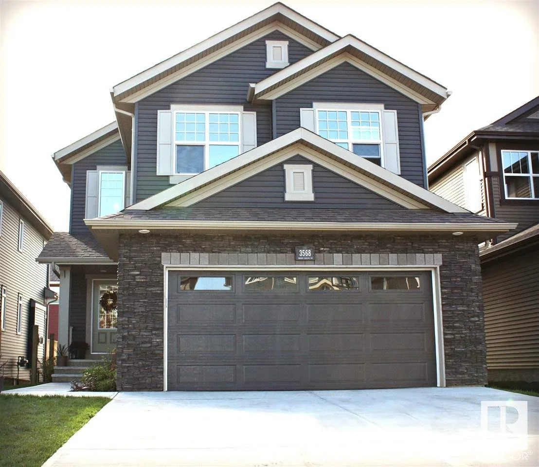 A modern two-story house with a dark gray garage door, stone facade, and blue siding with white trim windows and shutters.