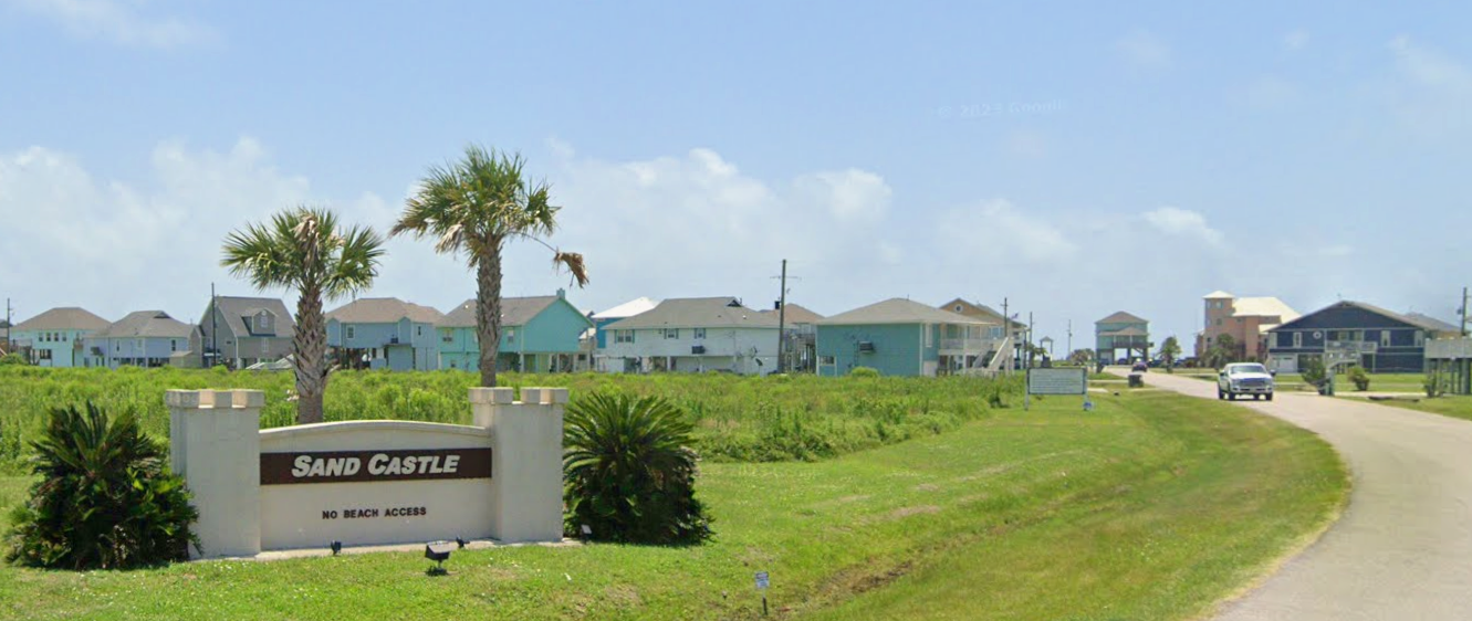 Beach houses in Sand Castle community with a sign indicating no beach access, palm trees, and a curved road.