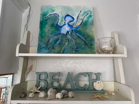 A wall shelf with a sea-themed decor display, including a blue octopus painting, large teal letters spelling 'BEACH', and various seashells and starfish.