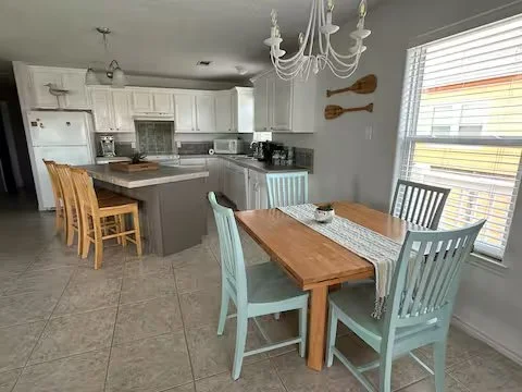 Dining area with a wooden table and chairs, a chandelier, and a kitchen with white cabinets and appliances.