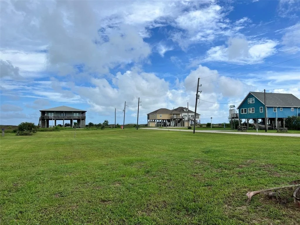 Three houses on stilts in a grassy area under a partly cloudy sky, with utility poles and a paved road in the scene.