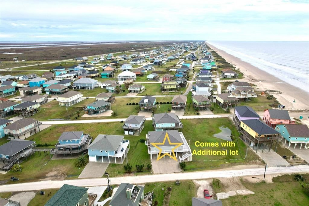 Aerial view of a beachside neighborhood with colorful houses, some on stilts, along the shoreline. Annotations indicate one property comes with an additional lot.