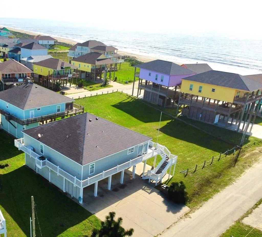 Colorful beach houses on stilts along the coast of a sandy beach, with ocean waves in the background.